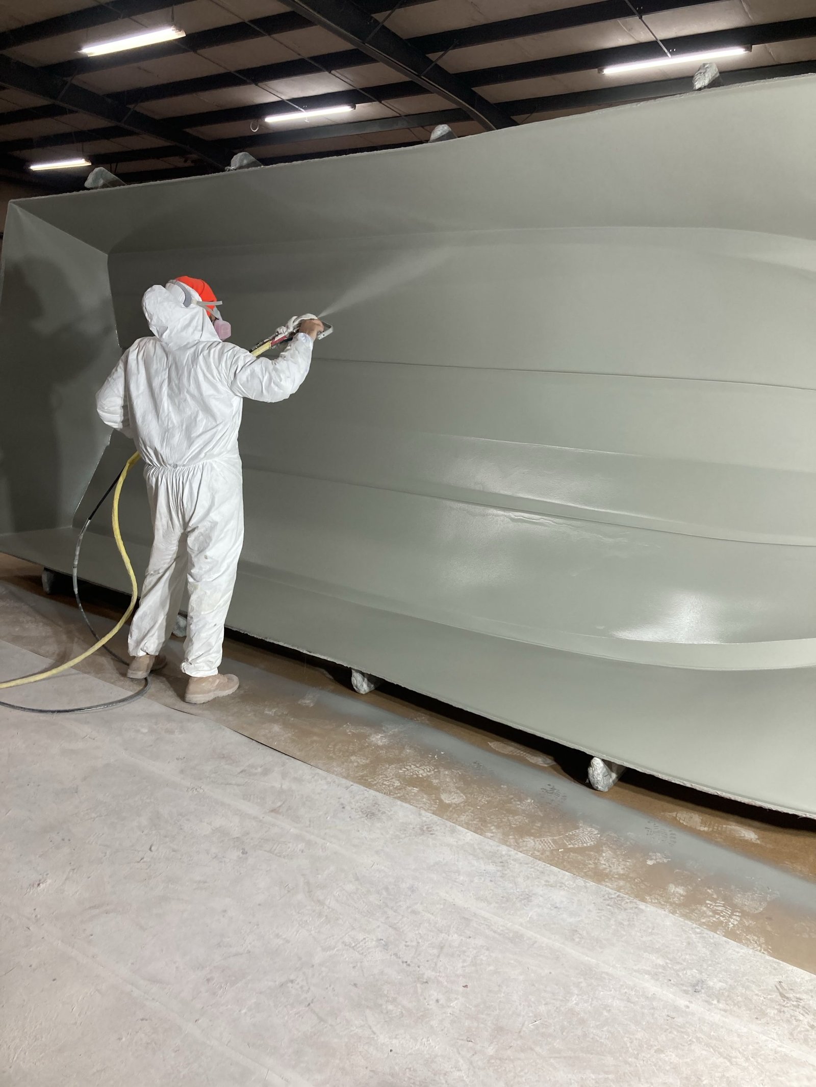 Worker spraying gelcoat inside a boat mold